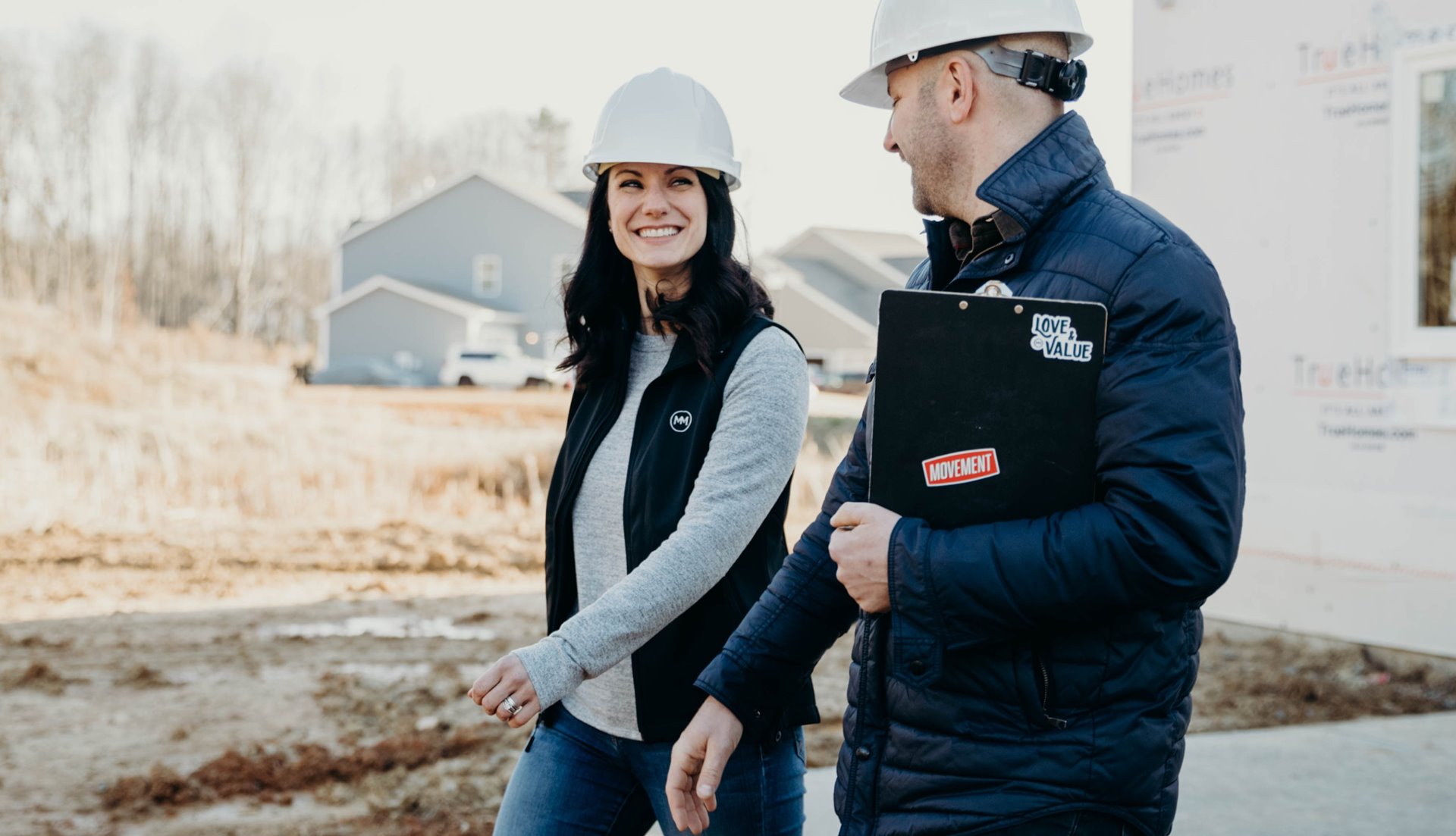 Man and woman with hardhats standing on land being developed for residential use