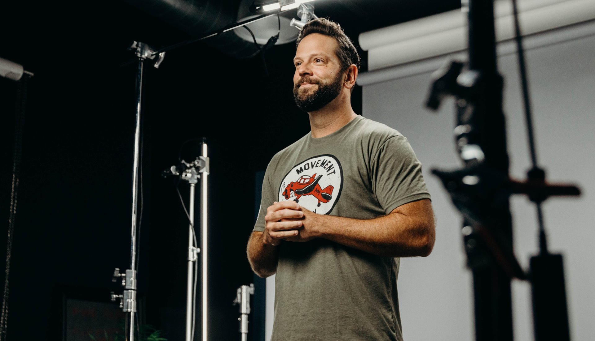 Man standing with hands together in front of him looking towards an off-screen camera